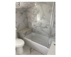 A white toilet sits next to a marble tiled shower.