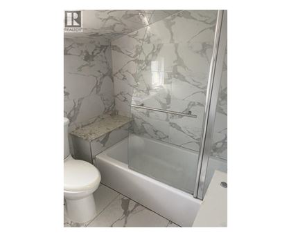 A white toilet sits next to a marble tiled shower.