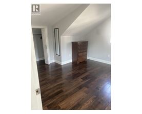 A room with wooden floors and a white wall with a mirror and a wooden chest of drawers.