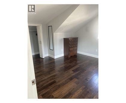 A room with wooden floors and a white wall with a mirror and a wooden chest of drawers.