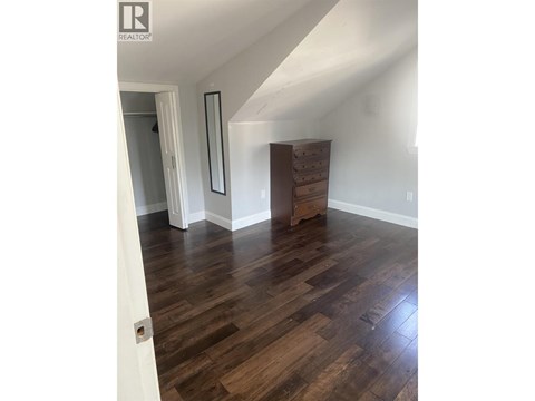 A room with wooden floors and a white wall with a mirror and a wooden chest of drawers.
