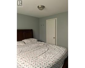 A bed with a white comforter with a pattern of red and black shapes is in a bedroom with a white door and a white ceiling light.