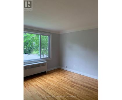 A room with wood flooring and a window overlooking a tree-filled street.