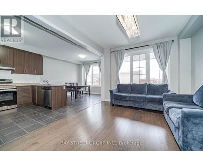 A spacious living room with a grey sofa and a kitchen area with wooden cabinets.