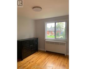 A room with a window showing a view of a house and trees.