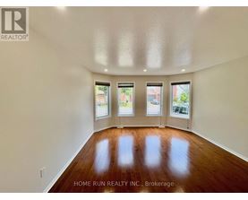 A spacious room with wooden floors and three windows.