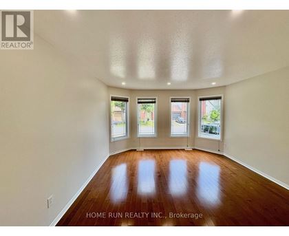 A spacious room with wooden floors and three windows.