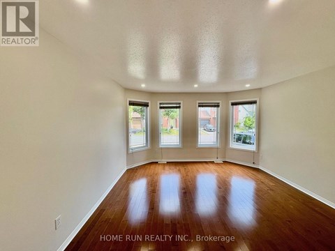 A spacious room with wooden floors and three windows.