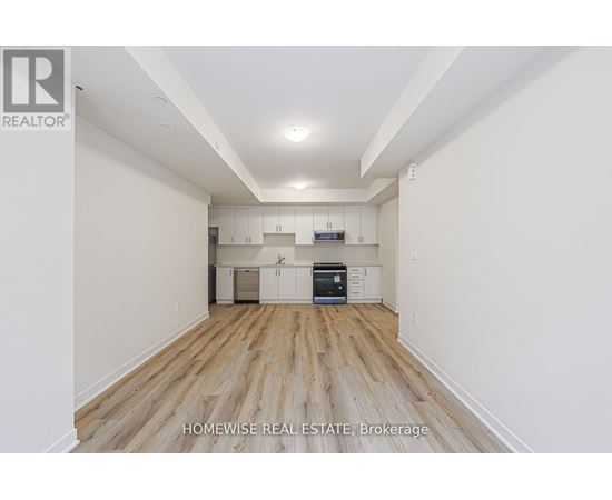 A spacious room with wooden flooring and white walls, featuring a kitchen area with cabinets and a countertop.