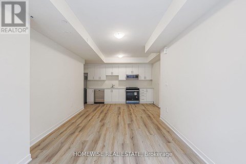 A spacious room with wooden flooring and white walls, featuring a kitchen area with cabinets and a countertop.