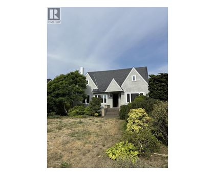 A house with a grey roof and white walls is surrounded by greenery.