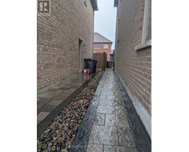 A narrow alley with a brick wall on one side and a gravel area on the other.