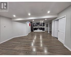 A spacious room with wooden flooring and a kitchen area in the background.
