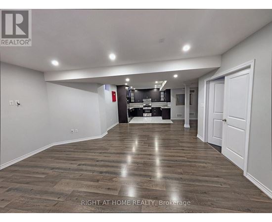 A spacious room with wooden flooring and a kitchen area in the background.
