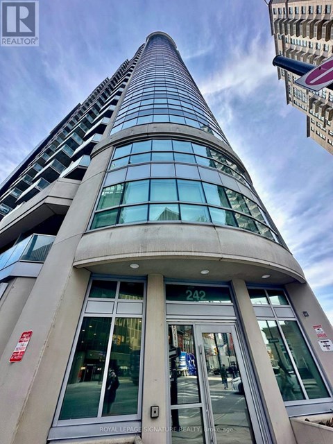 A tall building with a curved glass facade and a sign that reads "242" is seen from the street level.
