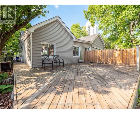 A wooden deck in front of a house with a fence and trees in the background.