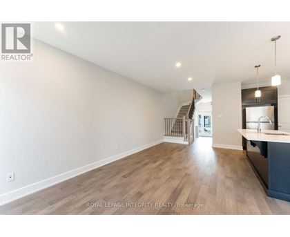 A spacious room with wooden flooring and a staircase in the background.