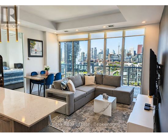 A living room with a grey couch and a large window overlooking a cityscape.
