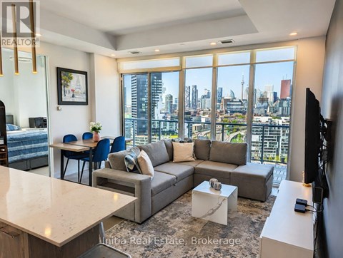 A living room with a grey couch and a large window overlooking a cityscape.