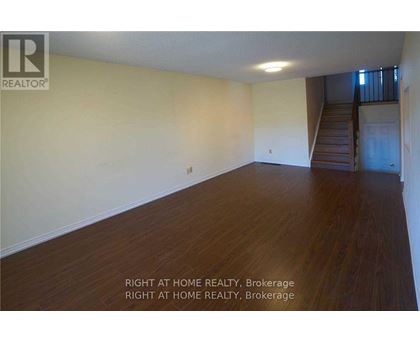 A room with wooden floors and a staircase in the background.