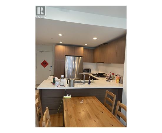 A kitchen with wooden chairs and a stainless steel refrigerator.