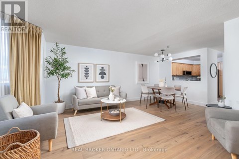 A well-lit living room with a grey sofa, a wooden coffee table, and a dining table with chairs.