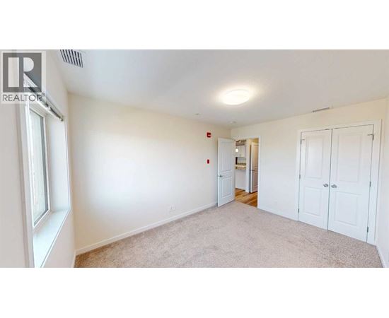 A white bedroom with a window and a door leading to another room.