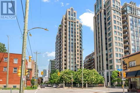 A city street with a tall building in the background and a REALTOR sign in the foreground.