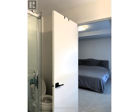 A white door is open to a bedroom with a bed and a toilet.