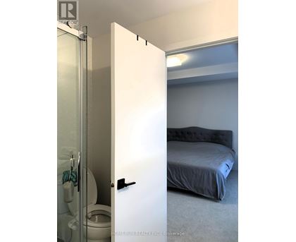 A white door is open to a bedroom with a bed and a toilet.