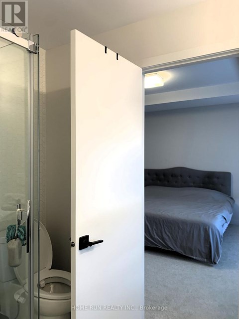 A white door is open to a bedroom with a bed and a toilet.