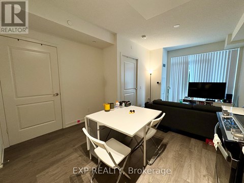 A living room with a white table and chairs, a black couch, and a television.