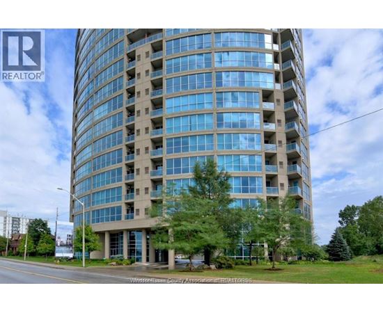 A tall building with many windows is surrounded by trees and grass.