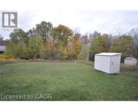 A white shed sits in a grassy field with trees in the background.