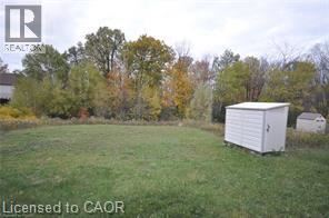 A white shed sits in a grassy field with trees in the background.