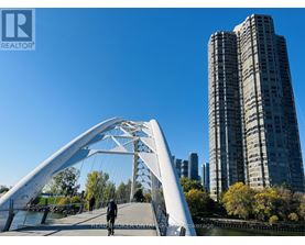 A person is walking on a bridge over a body of water with buildings in the background.