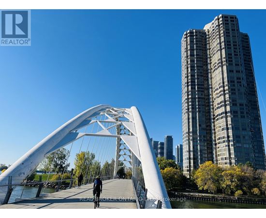 A person is walking on a bridge over a body of water with buildings in the background.