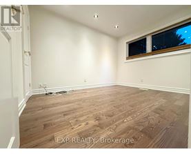 A room with wooden flooring and a window with a view of trees outside.