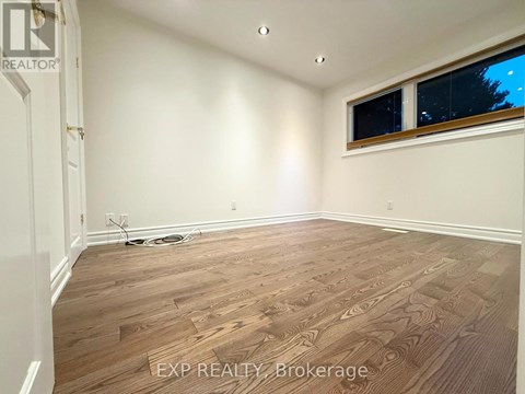 A room with wooden flooring and a window with a view of trees outside.