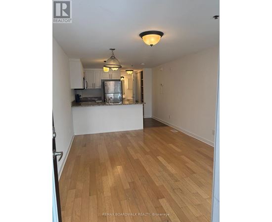 A room with wooden flooring and a kitchen area in the background.