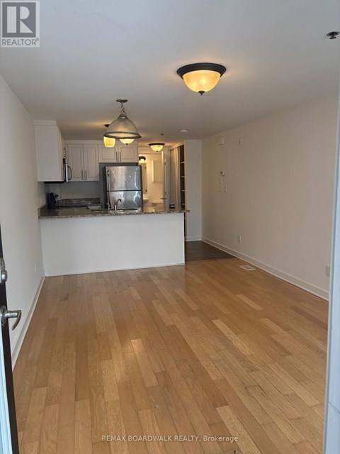 A room with wooden flooring and a kitchen area in the background.