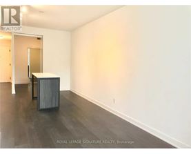 A room with a wooden floor and white walls, with a doorway leading to another room.