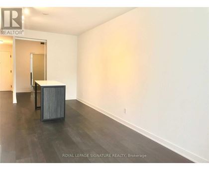 A room with a wooden floor and white walls, with a doorway leading to another room.