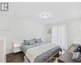 A bedroom with a bed, nightstand, and a window with white curtains.