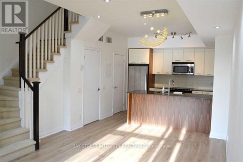 A well-lit kitchen with a bar counter and a staircase with wooden steps.