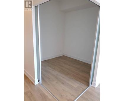 A room with a wooden floor and white walls, with a doorway open to another room.