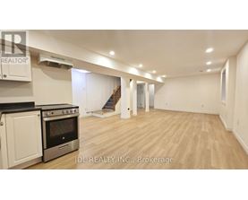 A spacious room with wooden flooring and a staircase in the background.