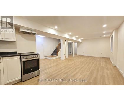 A spacious room with wooden flooring and a staircase in the background.
