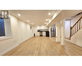 A spacious room with wooden flooring and a staircase on the right side.