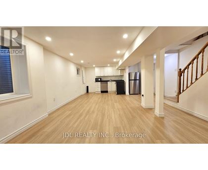 A spacious room with wooden flooring and a staircase on the right side.